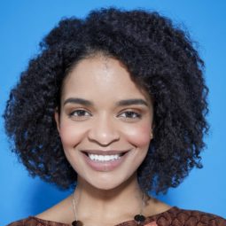 woman with natural curly hair in a bob length cut with a braid out style smiling at the camera