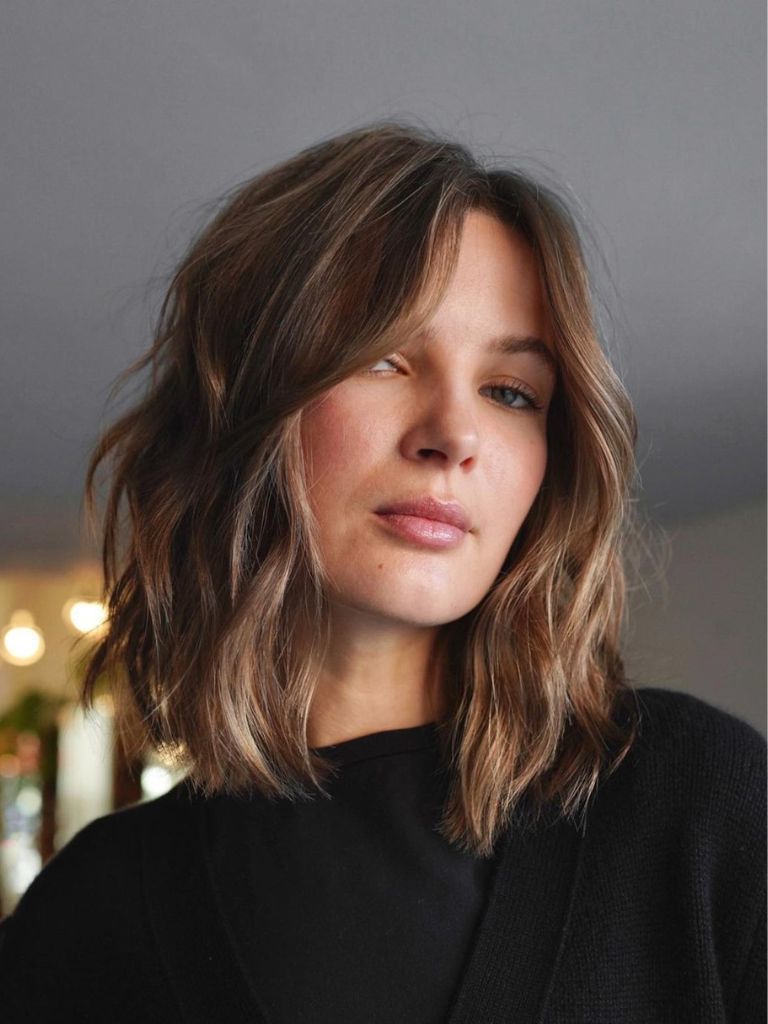 Woman with medium brown, long-layered choppy bob with blonde highlights wearing a black top.