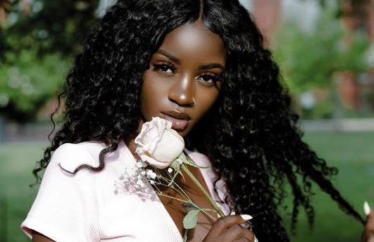 close up shot of woman with long mermaid curly weave hairstyle, wearing white rose and a pink top, posing outside