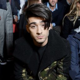 zayn malik sat down wearing a black and khaki coat with his dark brown hair worn in a side fringe